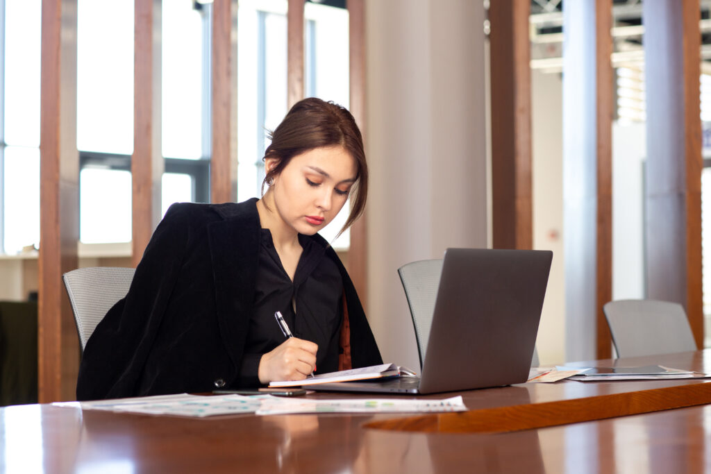 mujer joven escribiendo en su escritorio con pc al frente