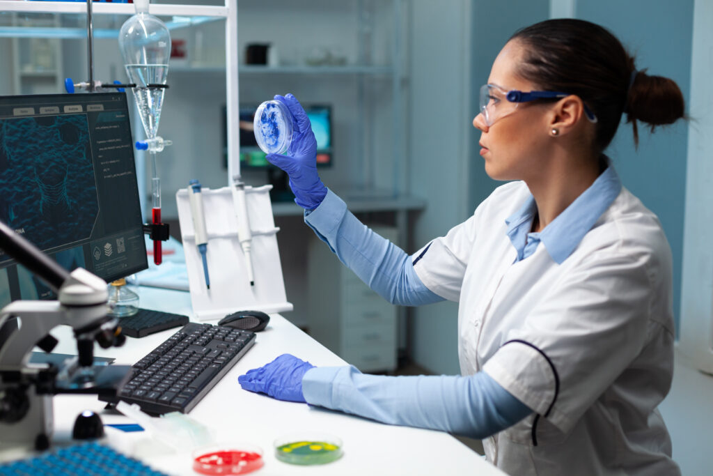 Biologist researcher woman holding transparent petri dish analyzing blue solution during biochemistry experiment. Scientist doctor working with dna sample in microbiology hospital laboratory