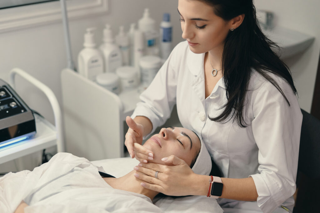 Beauty, spa and cosmetology concept. Young woman lies with closed eyes, cosmetologist making procedure for facial skin rejuvenation, facial massage.